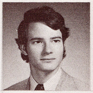 black and white headshot of young man in a light suit with a dark tie and short, wavy hair